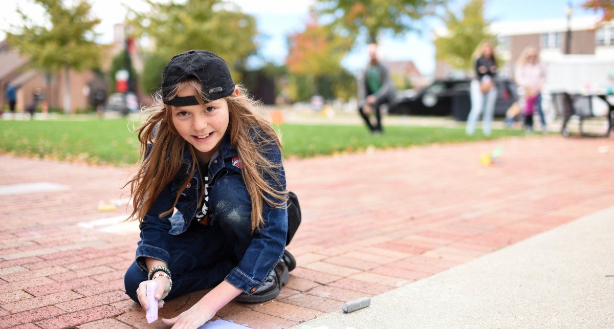 a young girl draws with chalk along the sidewalk at National Road Commons Park